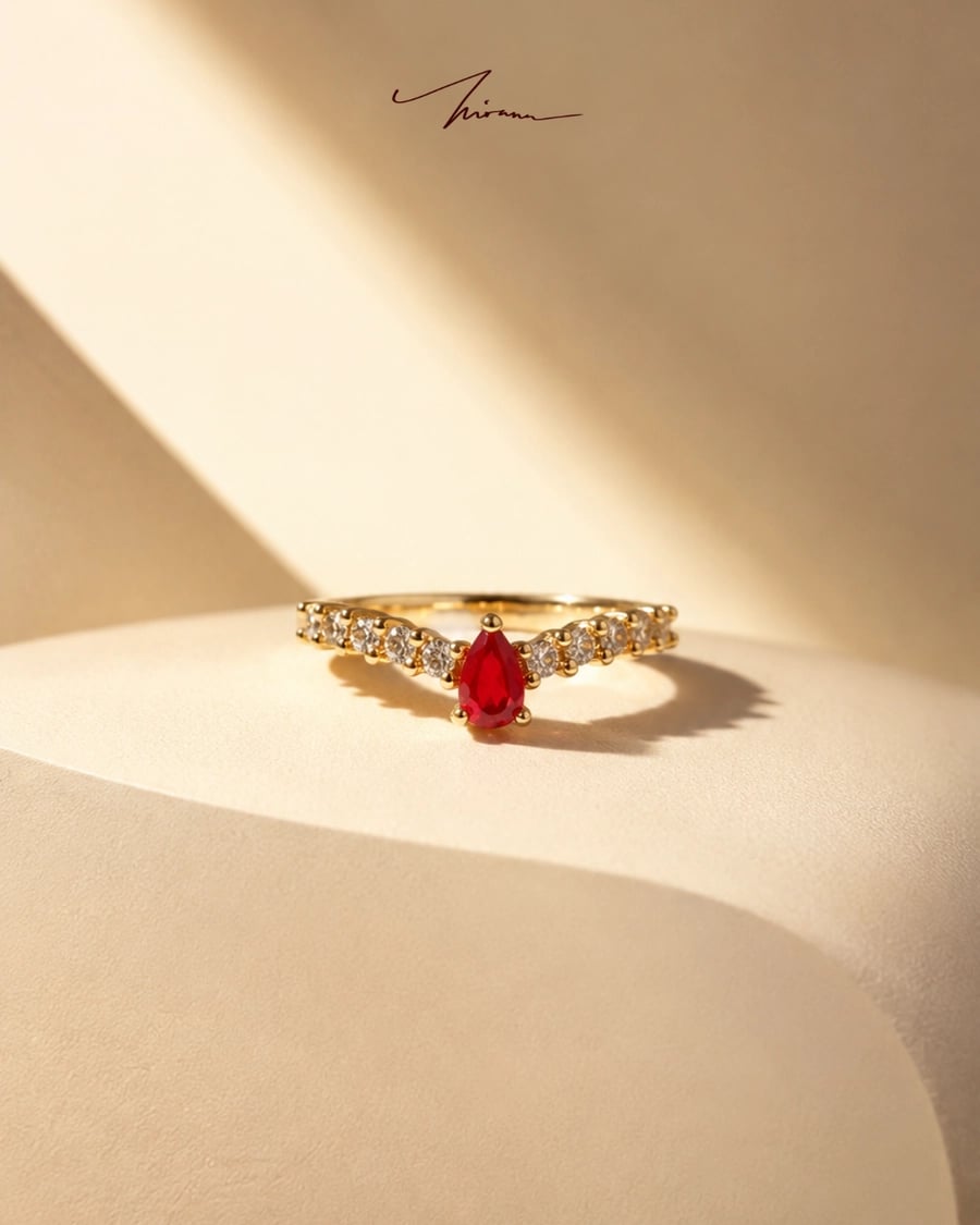 Cincin ruby pear-cut di atas suede krem dengan cahaya dramatis (Example)