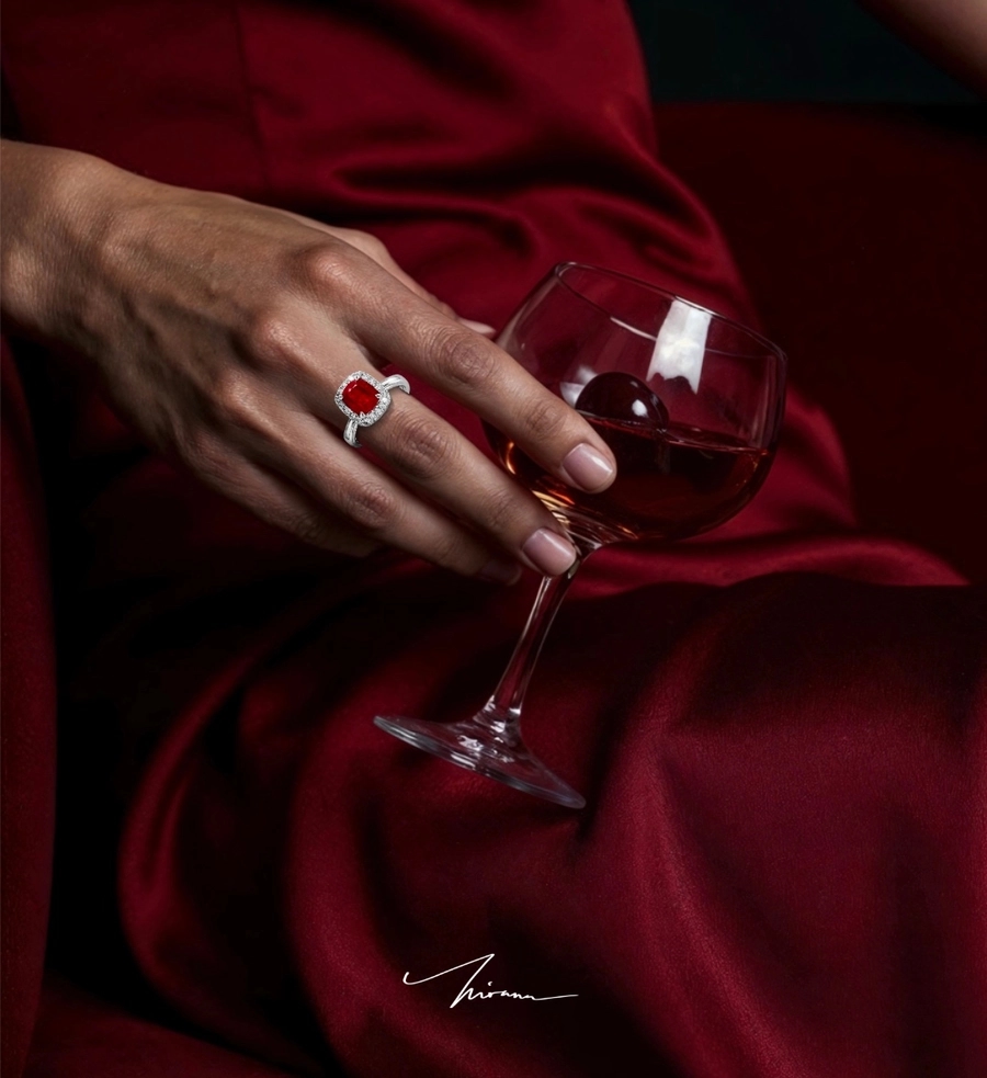 Cincin ruby di tangan memegang gelas anggur, latar sutra merah